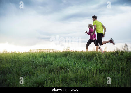 Vista laterale del determinato gli atleti in esecuzione sul campo erboso contro sky Foto Stock