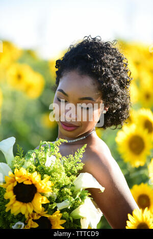 Close-up di sposa bouquet di contenimento mentre in piedi contro i girasoli presso l'azienda Foto Stock