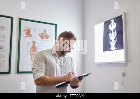Medico maschio scrittura permanente, mentre in clinica medica Foto Stock