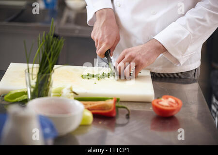 Close-up di chef tritare verdure sul tagliere in cucina commerciale Foto Stock