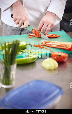 Sezione mediana dello chef tritare verdure sul tagliere in cucina commerciale Foto Stock