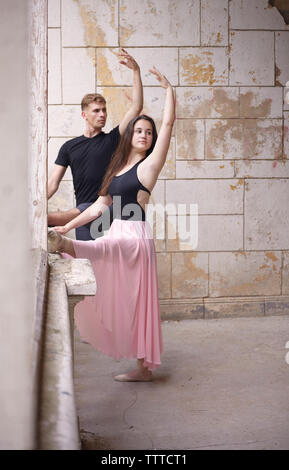 Gli amici con le braccia sollevate la pratica di balletto in vecchio edificio contro la parete Foto Stock