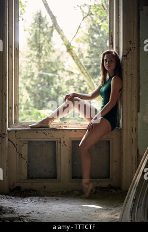 Vista laterale ritratto della ballerina seduta sul davanzale nel vecchio edificio Foto Stock