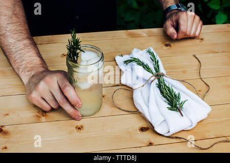 Sezione mediana di uomo con bicchiere di limonata con rosmarino a tavola Foto Stock