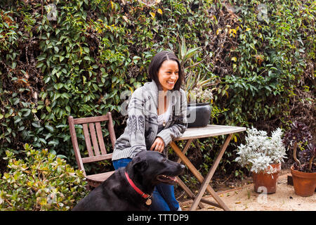 Donna sorridente seduto su una sedia da Labrador Retriever a backyard Foto Stock