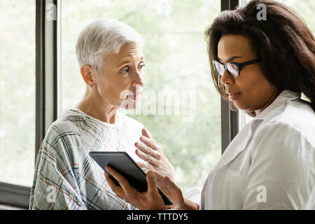 Medico donna spiegando relazione al paziente sulla tavoletta digitale in clinica Foto Stock