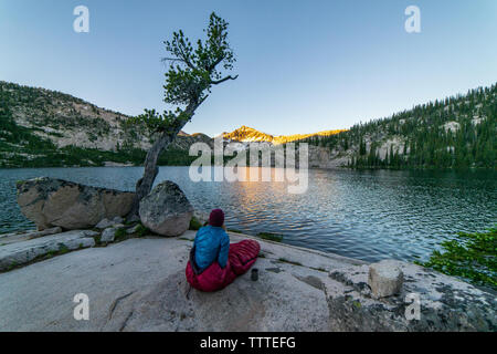 La donna nel sacco a pelo a lago alpino guardando alpenglow sunrise Foto Stock