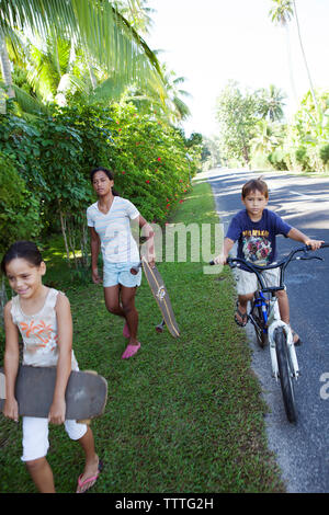 Polinesia Francese, Moorea. Bambini locali lo skateboard e mountain bike. Foto Stock