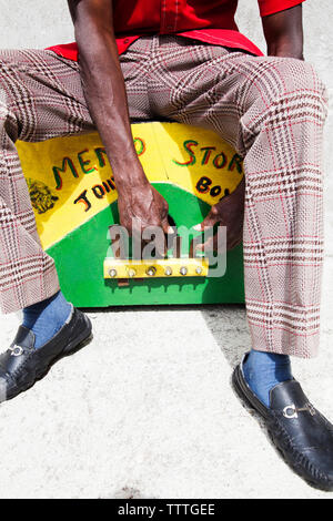 Giamaica, Port Antonio. Derrick "Johnny' Henry del Mento Band, il Jolly Boys, seduto e giocare la casella marumba. Foto Stock