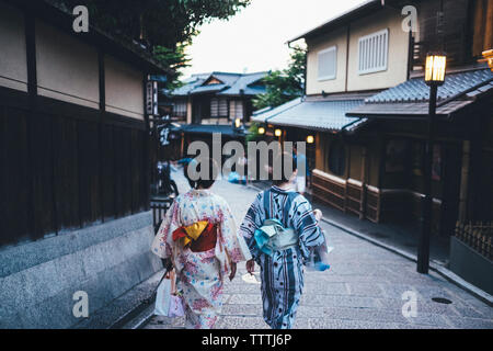 Vista posteriore delle donne in kimono camminando sul marciapiede nel mezzo di edifici residenziali Foto Stock