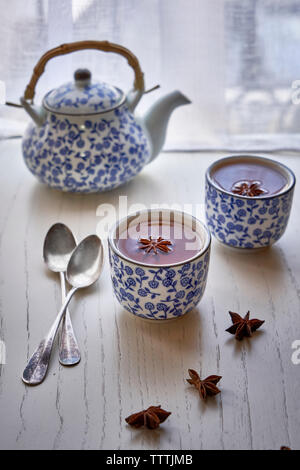 Cup a caldo con infusione di anice stellato e teiera in bianco su un tavolo di legno. Foto Stock