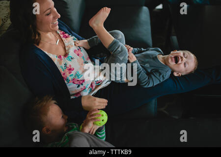 Elevato angolo di visione della madre a giocare con figli sul divano di casa Foto Stock