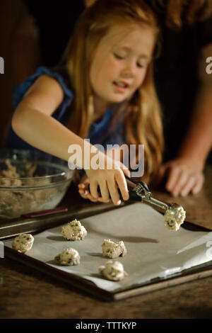 Ragazza di mettere pasta biscotto sulla teglia utilizzando serve scoop a casa Foto Stock