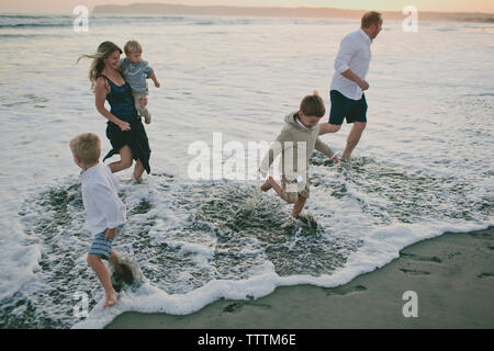 La famiglia felice giocando in onde in riva al mare durante il tramonto Foto Stock