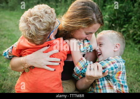 Felice madre giocando con figli mentre è seduto sul campo erboso in foresta Foto Stock