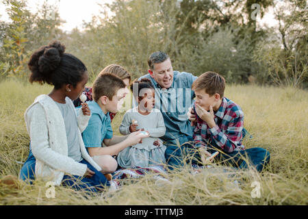 I genitori guardando i bambini aventi il cibo durante la seduta sul campo al park Foto Stock