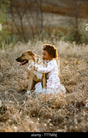 Vista laterale della ragazza con cane inginocchiato sul campo erboso a forest Foto Stock