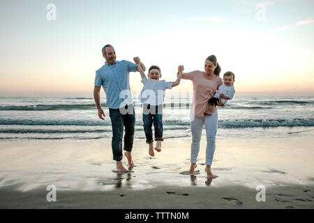 I genitori giocando con il figlio a beach contro sky durante il tramonto Foto Stock