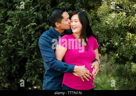 Amare luomo kissing donna incinta contro i rami in posizione di parcheggio Foto Stock