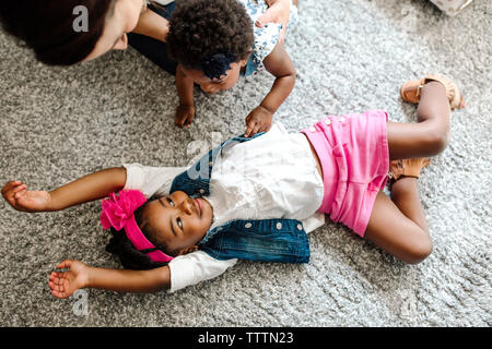 Elevato angolo di visione della madre con la figlia guardando ragazza distesa sul tappeto a casa Foto Stock