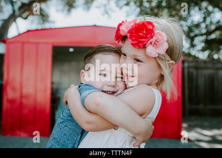 Ritratto di carino fratello abbracciando la sorella mentre in piedi contro la red garage in cantiere Foto Stock
