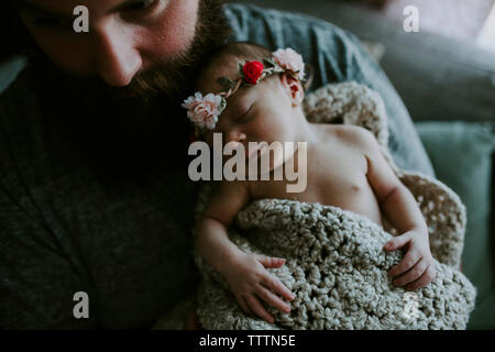 Elevato angolo di close-up di padre barbuto che trasportano carino sleeping figlia indossa tiara comodamente seduti sul divano di casa Foto Stock