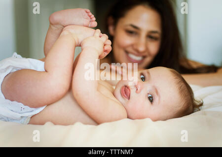 Felice madre guardando giocoso il bambino a letto Foto Stock