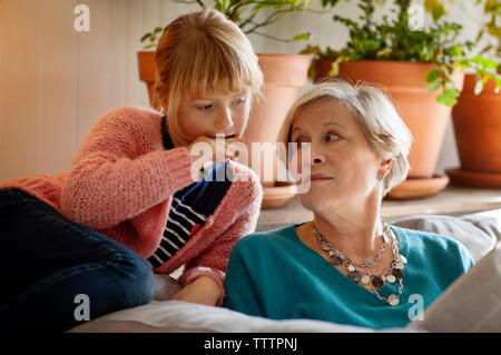 Nonna guardando il nipote rivista di lettura mentre è seduto sul divano Foto Stock
