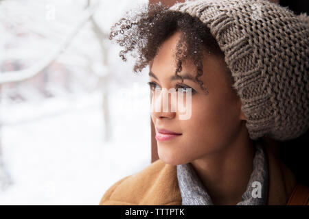 Close-up della donna che indossa knit hat guardando attraverso la finestra Foto Stock