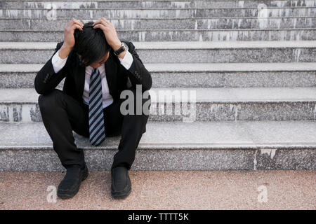 Gli imprenditori asiatici con mal di testa o emicrania presso il municipio dopo le immagini di lavoro di giovani imprenditori che sono stanchi, stress, crisi, depressione, failu Foto Stock