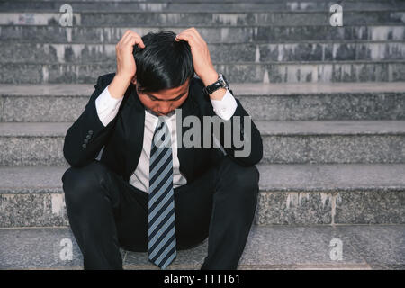 Gli imprenditori asiatici con mal di testa o emicrania presso il municipio dopo le immagini di lavoro di giovani imprenditori che sono stanchi, stress, crisi, depressione, failu Foto Stock