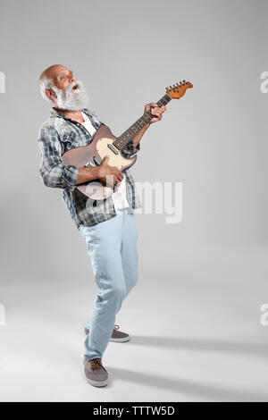 Senior uomo con la chitarra su muro grigio sfondo Foto Stock