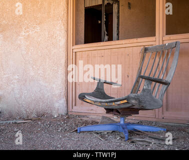 Un vecchio e stagionato telaio in legno blu e le gambe di una sedia per ufficio seduto davanti a un edificio abbandonato Foto Stock