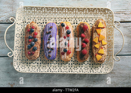 Deliziosi eclairs colorati con bacche e frutta sul vassoio Foto Stock