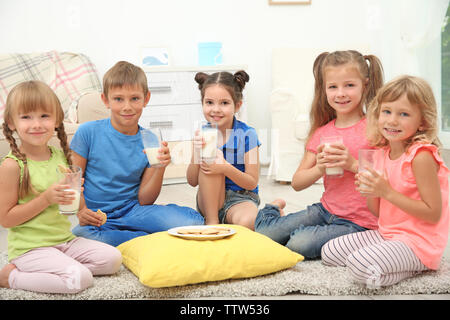 Bambini I cookie di mangiare e di bere latte mentre è seduto sul pavimento Foto Stock