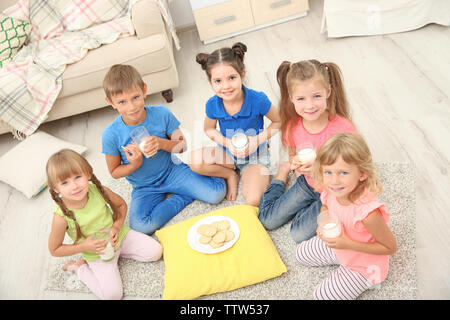 Bambini I cookie di mangiare e di bere latte mentre è seduto sul pavimento Foto Stock