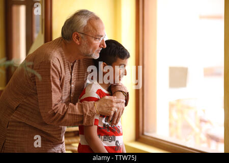 Indian uomo vecchio con il suo nipote guardando attraverso la finestra di uscita Foto Stock