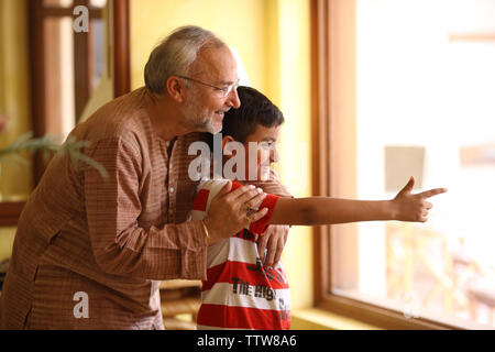 Indian uomo vecchio con il suo nipote guardando attraverso la finestra di uscita Foto Stock