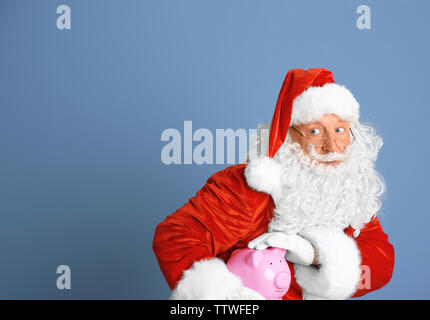 Santa Claus holding salvadanaio su sfondo blu Foto Stock