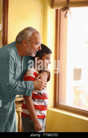 Indian uomo vecchio con il suo nipote guardando fuori attraverso la finestra Foto Stock