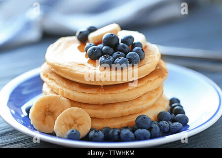 Piastra con gustosi pancake, fette di banana e le bacche sul tavolo di legno, vista ravvicinata Foto Stock