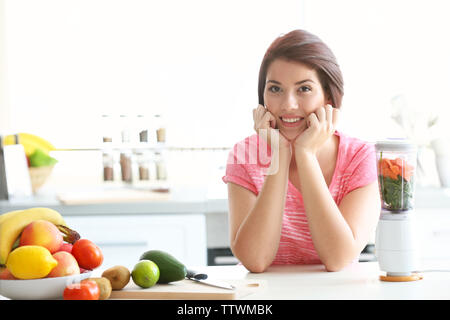 Giovane bella donna che fa con succo di frutta e verdura in cucina Foto Stock