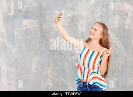 Attraente ragazza adolescente tenendo selfie su sfondo grigio Foto Stock