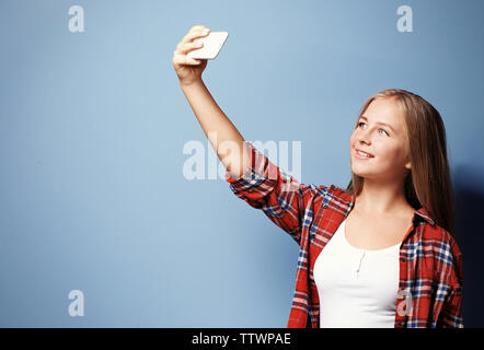 Carina ragazza adolescente tenendo selfie su sfondo blu Foto Stock