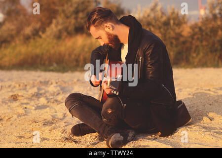 Uomo bello con la chitarra sulla spiaggia Foto Stock