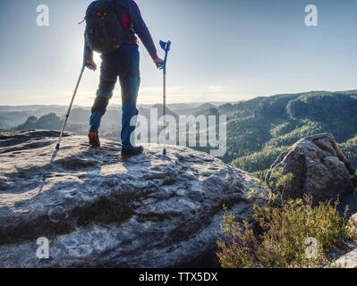 Hurt uomo forte in piedi con le stampelle sul vertice di montagna. Uomo anziano a piedi con aiuto di avambraccio stampelle pur esprimendo di felicità della libertà. Foto Stock