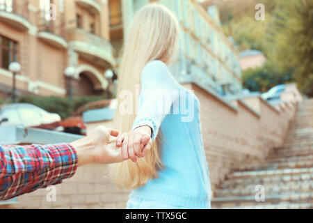 Follow-me concetto. Giovane donna azienda mano d'uomo sulla strada sfondo scale Foto Stock