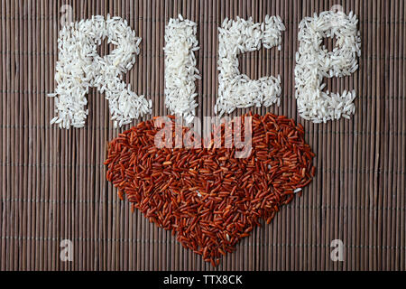 Parola di riso e forma di cuore realizzata con diversi tipi di grani sul tappetino di bambù sfondo Foto Stock