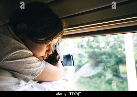 Carino ragazza distesa sul ripiano più in alto in treno e guardando fuori dalla finestra Foto Stock