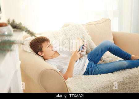 Carino schoolboy leggendo un libro sul divano Foto Stock